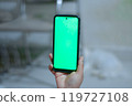 Hand Holding Smartphone with Green Screen in Indoor Setting 119727108