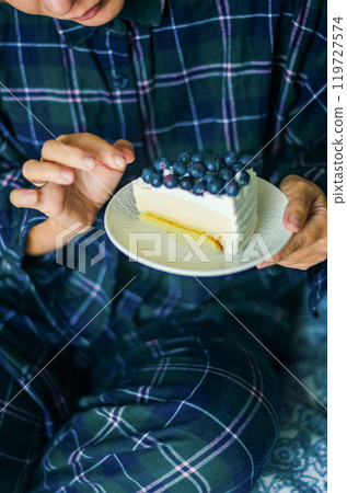 woman eating a Cheesecake in Pajamas for a Cozy Dessert Moment in bedroom . High quality photo 119727574