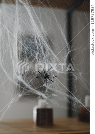 Happy Halloween concept. White fake white wool spiderweb. Scary spiders, candles, bats. Interior of festive living room with scary Halloween decorations 119727984
