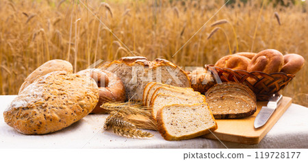 Lot of different flavored bread, wheat, rye, on the table in the field outside 119728177