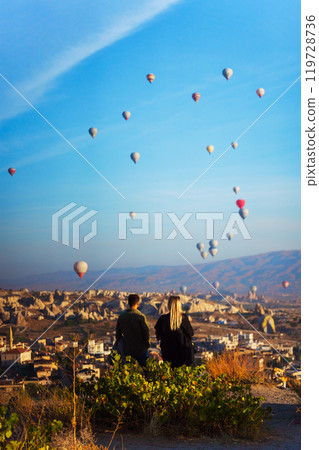 A man and a woman watch hot air balloons over a city in Cappadocia A man and a woman watch hot air balloons over a city in Cappadocia 119728736