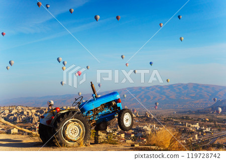 A blue tractor sits on a hill with hot air balloons flying behind 119728742