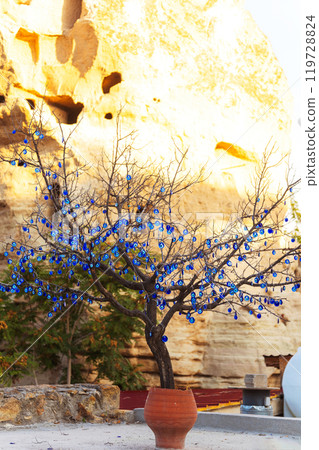 There is a beautiful tree placed in a pot adorned with blue glasses devil eyes.  119728824