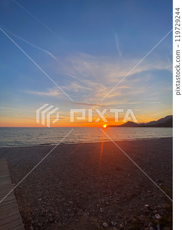 Breathtaking view of a sunset over a tranquil beach creates a peaceful seaside atmosphere. The warm glow of the sun reflecting on the water enhances the natural beauty of the horizon 119729244