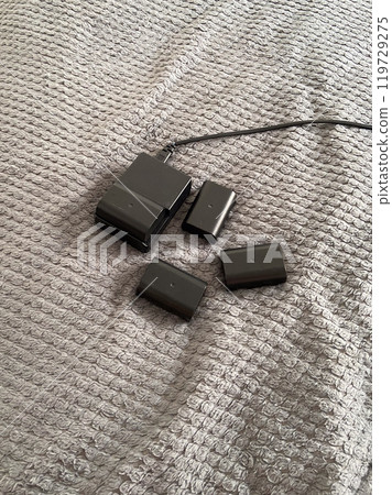 Set of camera batteries and a charger lie neatly arranged on a textured gray surface, ready for use. This image portrays a sense of preparation and practicality in the world of photography Set of camera batteries and a charger lie neatly arranged on a textured gray surface, ready for use. This image portrays a sense of preparation and practicality in the world of photography 119729275