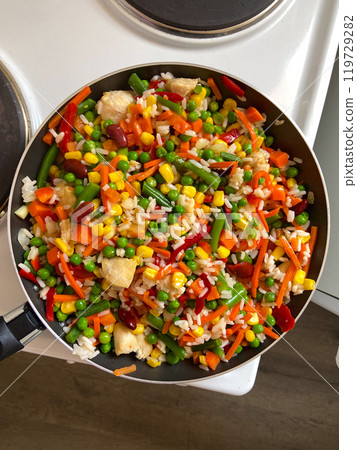 Vibrant stir-fry of colorful vegetables and rice in a pan creates a lively and delicious visual feast. The dish's bright hues and variety of ingredients highlight the joy and creativity of cooking at 119729282