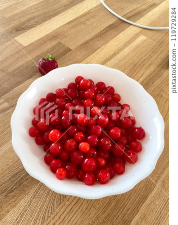 Collection of vibrant red berries sits elegantly in a white bowl, creating a striking contrast against a wooden background. Simple composition showcases the freshness and natural appeal of the fruit 119729284
