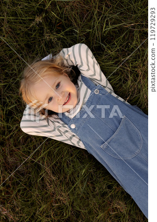 A young girl is laying on the grass, smiling and looking up at the camera 119729293