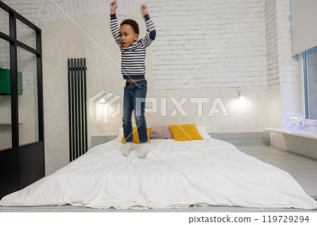 Kid jumping on the bed and looking enjoyed and contented Kid jumping on the bed and looking enjoyed and contented 119729294