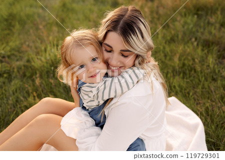 A woman is holding a baby girl in a grassy field A woman is holding a baby girl in a grassy field 119729301