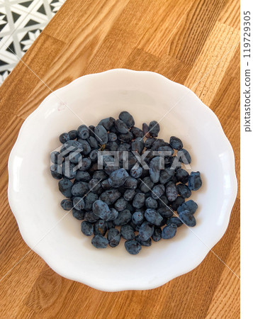 White bowl filled with freshly picked haskap berries sits prominently on a wooden table, exuding a rustic charm. The dark, rich color of the berries contrasts beautifully with the bright bowl and 119729305