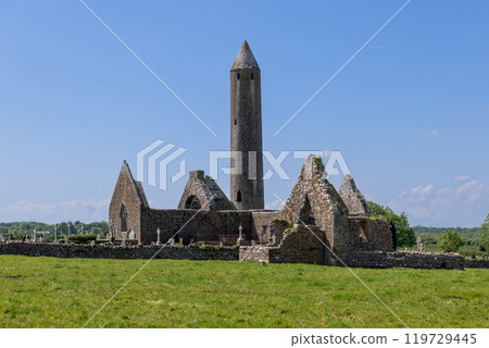 Kilmacduagh Abbey ruins in Galway with tall round tower ancient stone church surrounded by fields 119729445