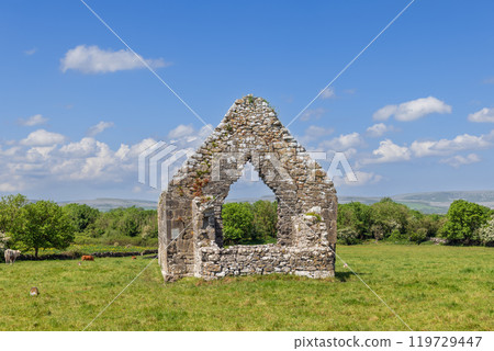 Ancient stone arch at Kilmacduagh Abbey stands alone in green field under blue sky Ancient stone arch at Kilmacduagh Abbey stands alone in green field under blue sky 119729447