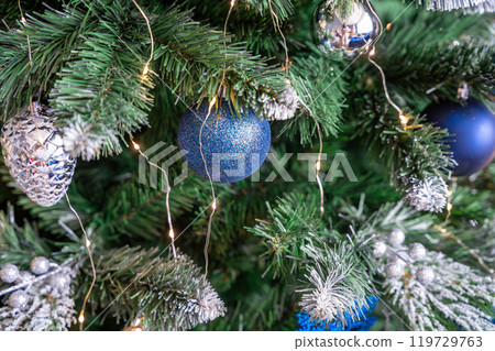 Christmas tree with blue and silver toys. Festively decorated Christmas tree with garlands. Symbol of the new year in trend colors 119729763