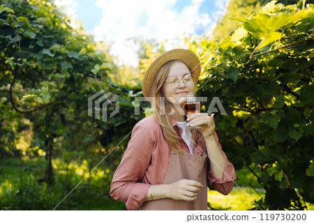 Professional woman sommelier testing pink wine in wine glass with tasting and smelling outdoors during sunset in a vineyard.  Professional woman sommelier testing pink wine in wine glass with tasting and smelling outdoors during sunset in a vineyard.  119730200