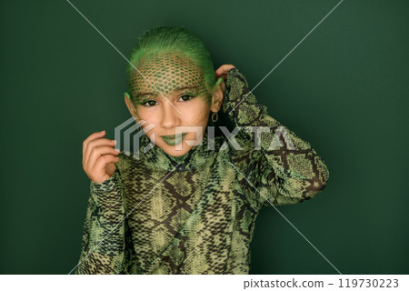 A teenage girl in the guise of a snake, with a face painted with paints and hair dyed green. The symbol of the New Year 2025 A teenage girl in the guise of a snake, with a face painted with paints and hair dyed green. The symbol of the New Year 2025 119730223