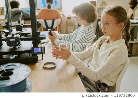 Children learning and engaging with advanced technology in educational setting, surrounded by gadgets and 3D printer. They are focused on their tasks and actively participating in the activity Children learning and engaging with advanced technology in educational setting, surrounded by gadgets and 3D printer. They are focused on their tasks and actively participating in the activity 119731900