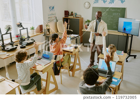 Teacher explaining lesson to attentive students in modern classroom setting. Students interacting with teacher, engaging actively in learning process Teacher explaining lesson to attentive students in modern classroom setting. Students interacting with teacher, engaging actively in learning process 119732005