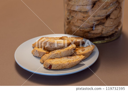 Almond cantucci cookies on white plate with full jar behind showcasing traditional Italian biscotti 119732395