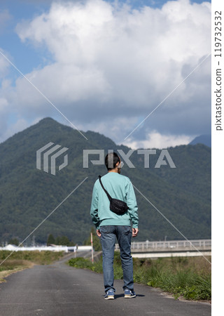 一個男人站在鄉間小路上的後視圖 119732532