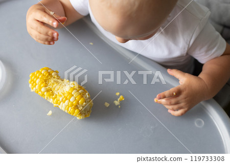 Baby eating sweet corn kernels from the table. Top view. 119733308