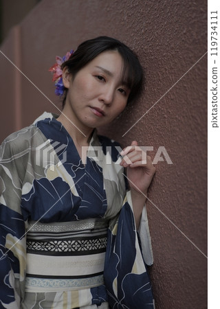 一位穿著浴衣的年輕女子站在棕色的牆上 一位穿著浴衣的年輕女子站在棕色的牆上 119734111