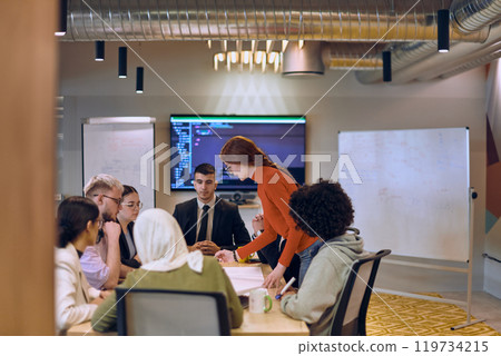 A diverse team of business experts in a modern glass office, attentively listening to a colleague's presentation, fostering collaboration and innovation. 119734215