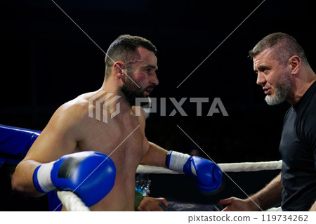 Cornered boxer receives strategic advice from trainer during intense bout. 119734262