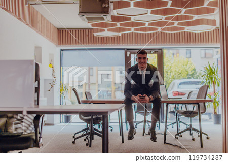 A businessman sitting on his desk, taking a moment to rest and unwind from a demanding workday, displaying a sense of tranquility and relaxation amidst the corporate environment A businessman sitting on his desk, taking a moment to rest and unwind from a demanding workday, displaying a sense of tranquility and relaxation amidst the corporate environment 119734287
