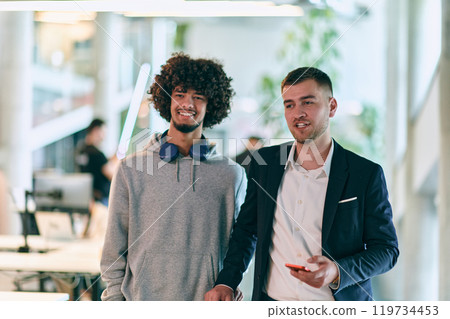 In a modern startup office setting, a business director and a young African American entrepreneur sit surrounded by their colleagues, embodying diversity and teamwork in the corporate world. In a modern startup office setting, a business director and a young African American entrepreneur sit surrounded by their colleagues, embodying diversity and teamwork in the corporate world. 119734453