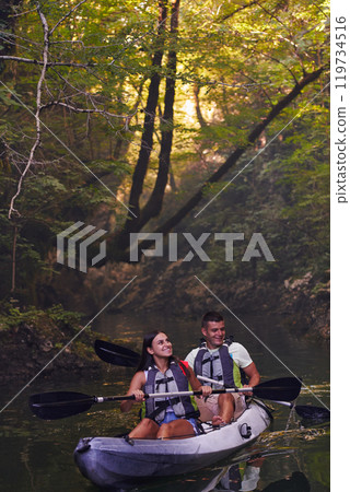 A young couple enjoying an idyllic kayak ride in the middle of a beautiful river surrounded by forest greenery 119734516