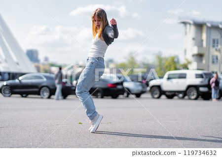 Young woman dancing joyfully in a parking lot during daytime Young woman dancing joyfully in a parking lot during daytime 119734632