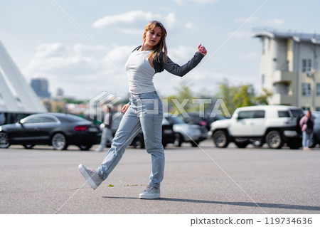 Young woman dancing in a parking lot on a sunny day with urban backdrop Young woman dancing in a parking lot on a sunny day with urban backdrop 119734636