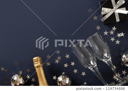 Composition with New Year champagne, drinking straws, shiny silver disco balls on blue navy background. View from above. Festive greeting card or invitation for party with copy space. Composition with New Year champagne, drinking straws, shiny silver disco balls on blue navy background. View from above. Festive greeting card or invitation for party with copy space. 119734886