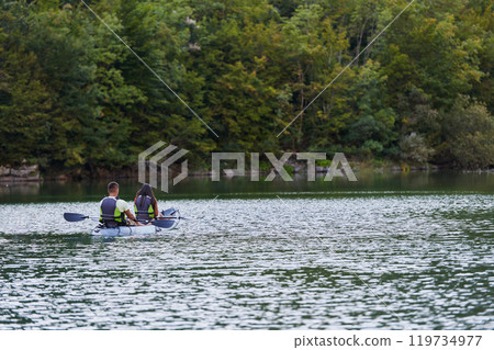 A young couple enjoying an idyllic kayak ride in the middle of a beautiful river surrounded by forest greenery 119734977
