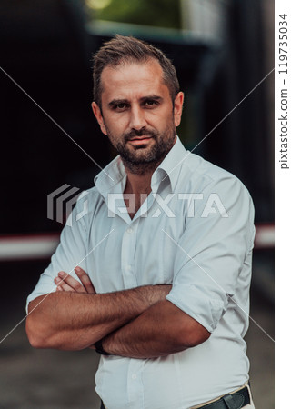A successful businessman in a white shirt with crossed arms posing outdoors 119735034