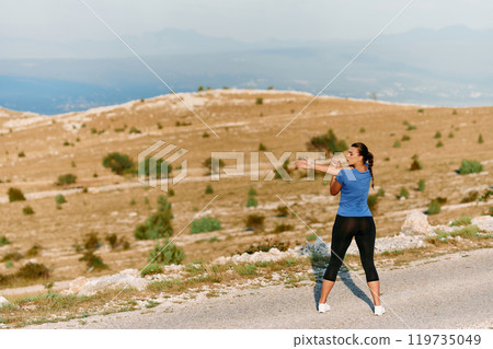 Determined Female Athlete Stretching After an Intense Run Through Rugged Mountain Terrain. 119735049