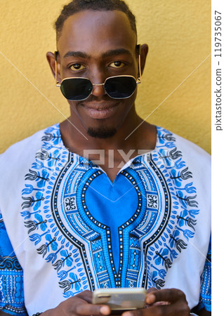 African American Teenager in Traditional Sudanese Attire Engaged with Smartphone African American Teenager in Traditional Sudanese Attire Engaged with Smartphone 119735067