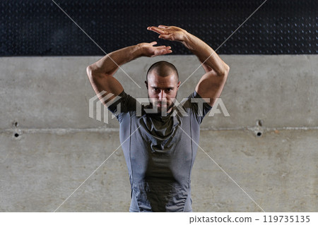 A muscular man working stretching exercises for his arms and body muscles in modern gym A muscular man working stretching exercises for his arms and body muscles in modern gym 119735135