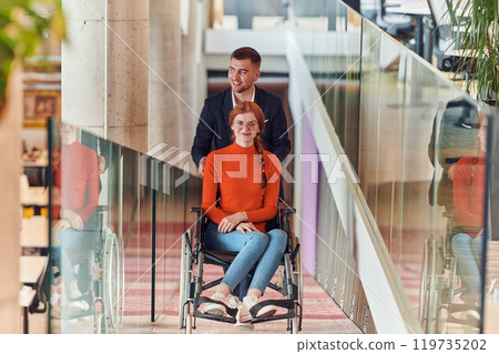 A company director assists his business colleague in a wheelchair, helping her navigate to their startup office, where they work alongside their diverse team of colleagues, emphasizing inclusivity and A company director assists his business colleague in a wheelchair, helping her navigate to their startup office, where they work alongside their diverse team of colleagues, emphasizing inclusivity and 119735202