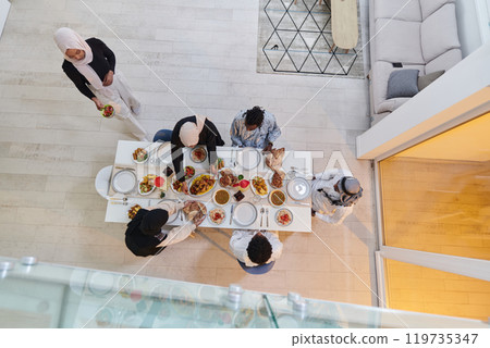 Top view of a Muslim family joyously comes together around a table, eagerly awaiting the communal iftar, engaging in the preparation of a shared meal, and uniting in anticipation of a collective Top view of a Muslim family joyously comes together around a table, eagerly awaiting the communal iftar, engaging in the preparation of a shared meal, and uniting in anticipation of a collective 119735347