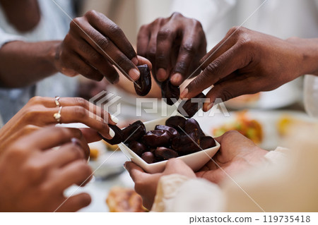 In a poignant close-up, the diverse hands of a Muslim family delicately grasp fresh dates, symbolizing the breaking of the fast during the holy month of Ramadan, capturing a moment of cultural unity In a poignant close-up, the diverse hands of a Muslim family delicately grasp fresh dates, symbolizing the breaking of the fast during the holy month of Ramadan, capturing a moment of cultural unity 119735418