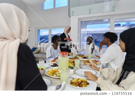 In the sacred month of Ramadan, a Muslim family joyously comes together around a table, eagerly awaiting the communal iftar, engaging in the preparation of a shared meal, and uniting in anticipation 119735516