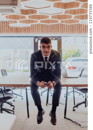 A businessman sitting on his desk, taking a moment to rest and unwind from a demanding workday, displaying a sense of tranquility and relaxation amidst the corporate environment A businessman sitting on his desk, taking a moment to rest and unwind from a demanding workday, displaying a sense of tranquility and relaxation amidst the corporate environment 119735566