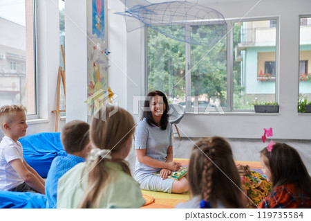 A happy female teacher sitting and playing hand games with a group of little schoolchildren 119735584