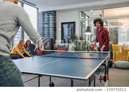 Business colleagues take a break from work to enjoy a game of table tennis, fostering teamwork and camaraderie in the workplace 119735612