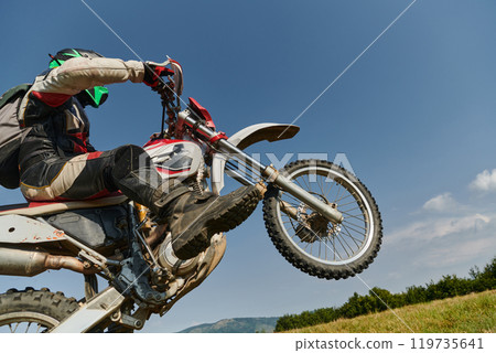 A fearless professional motocross rider skillfully executes an extreme back wheelie maneuver through a perilous forest terrain, showcasing remarkable balance and daring expertise A fearless professional motocross rider skillfully executes an extreme back wheelie maneuver through a perilous forest terrain, showcasing remarkable balance and daring expertise 119735641