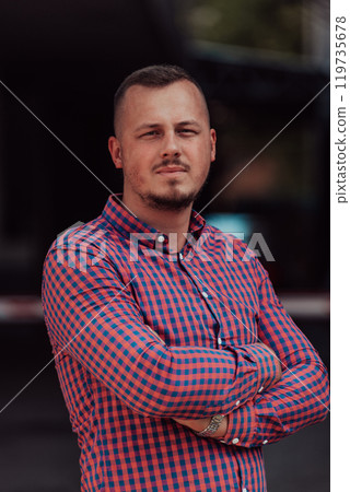 A successful young businessman in a shirt, with crossed arms, poses outdoors, confident expression on his face. A successful young businessman in a shirt, with crossed arms, poses outdoors, confident expression on his face. 119735678