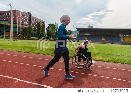 A Muslim woman in a burqa running together with a woman in a wheelchair on the marathon course, preparing for future competitions. A Muslim woman in a burqa running together with a woman in a wheelchair on the marathon course, preparing for future competitions. 119735695