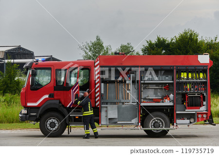 A firefighter meticulously prepares a modern firetruck for a mission to evacuate and respond to dangerous situations, showcasing the utmost dedication to safety and readiness in the face of a fire 119735719
